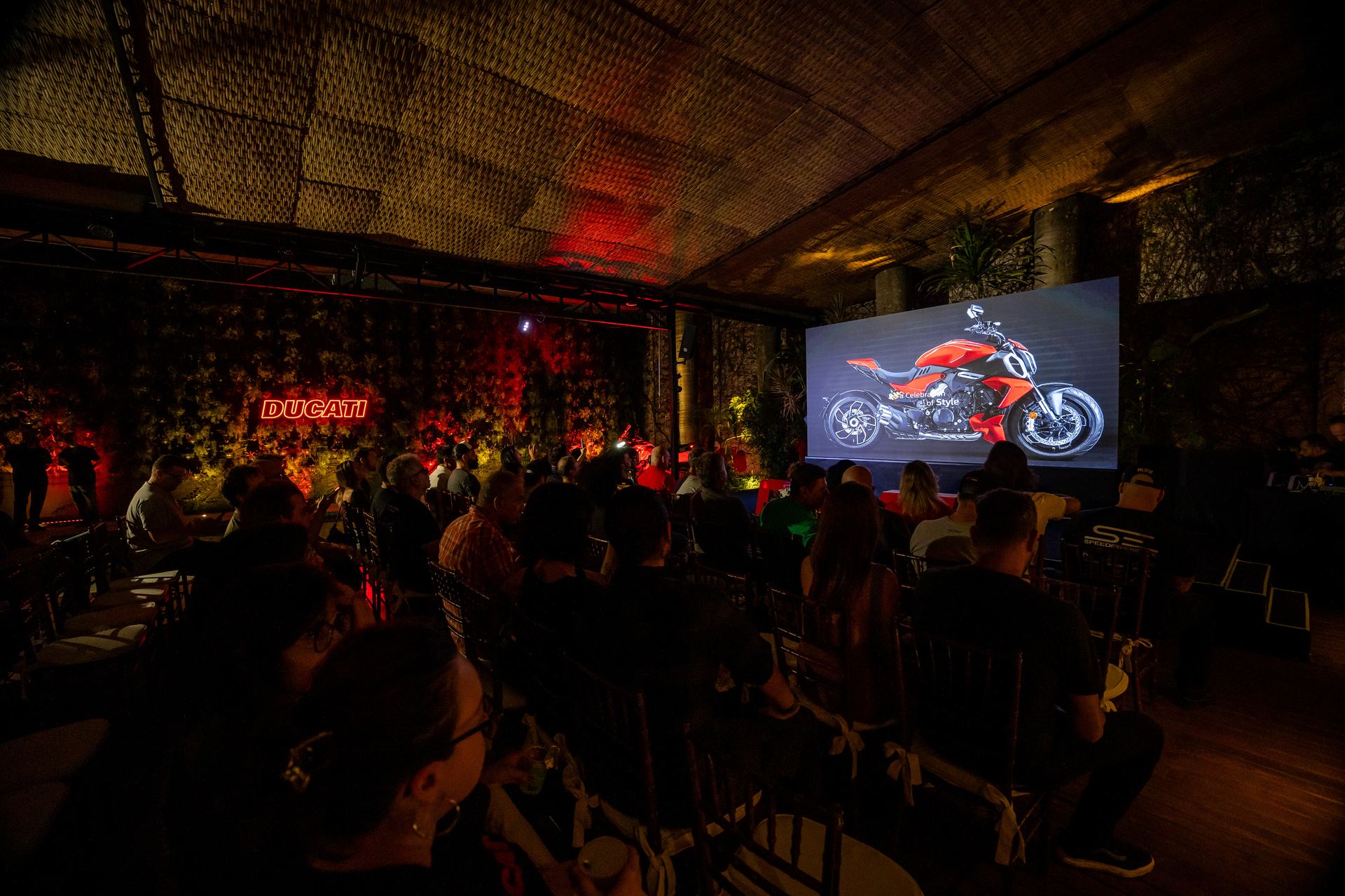 Vista panorâmica do lançamento estático da Ducati — painel neon e Diavel na tela