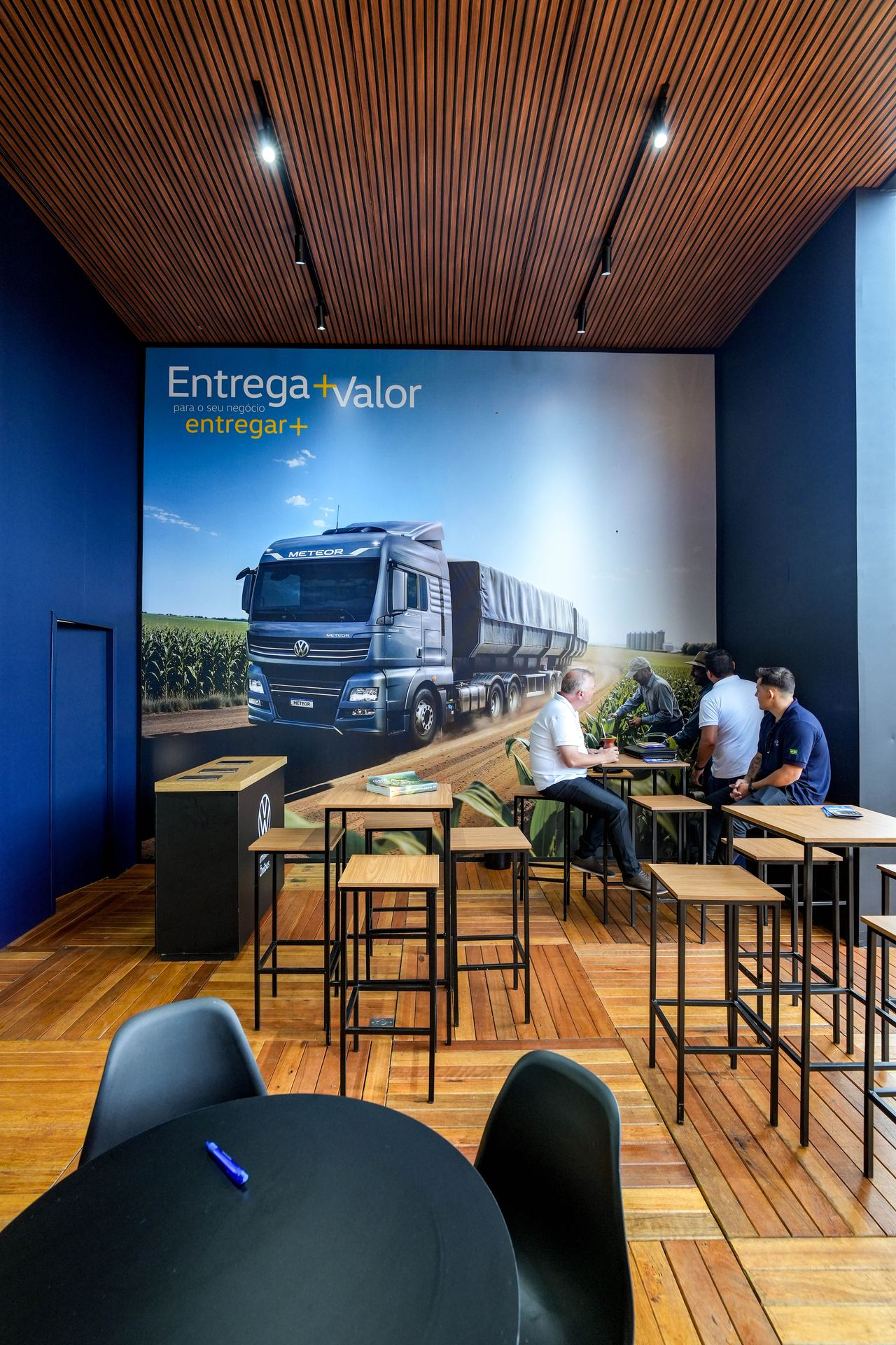 Visitantes no interior do estande VWCO — área de reunião com mural Meteor
